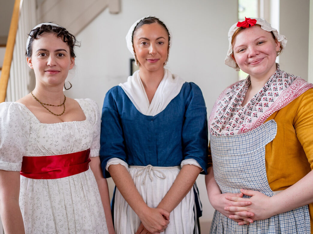 Three women dressed in traditional 18th century dresses pose for a photo at the Betsy Ross House in Philadelphia.