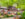 People sit at picnic tables in a beer garden surrounded by green trees and a brick wall spray painted with graffiti.