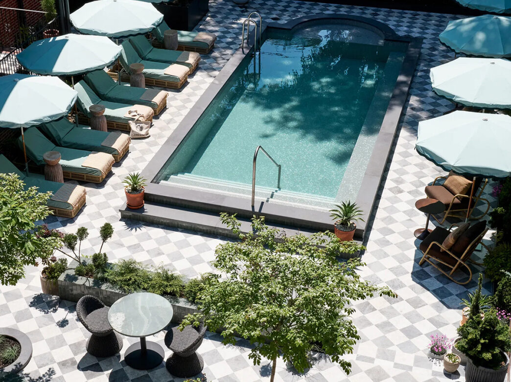 A courtyard pool with a gray and white tile pool deck is surrounded by teal lounge chairs and umbrellas at Hotel Anna & Bel.