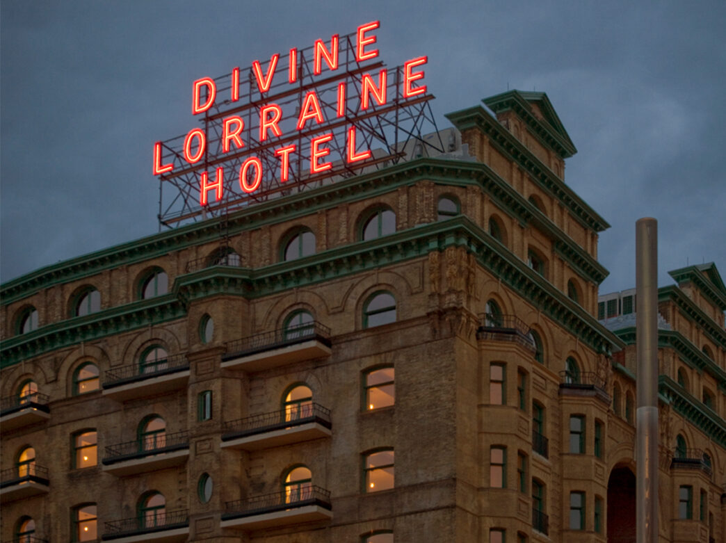 Exterior de un edificio marrón con un suspiro de neón rojo del Hotel Divine Lorraine por la noche.
