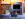 The camera faces a built in fireplace with a TV mounted above it and a reclaimed wood sliding door looking into a bathroom with a soaker tub.