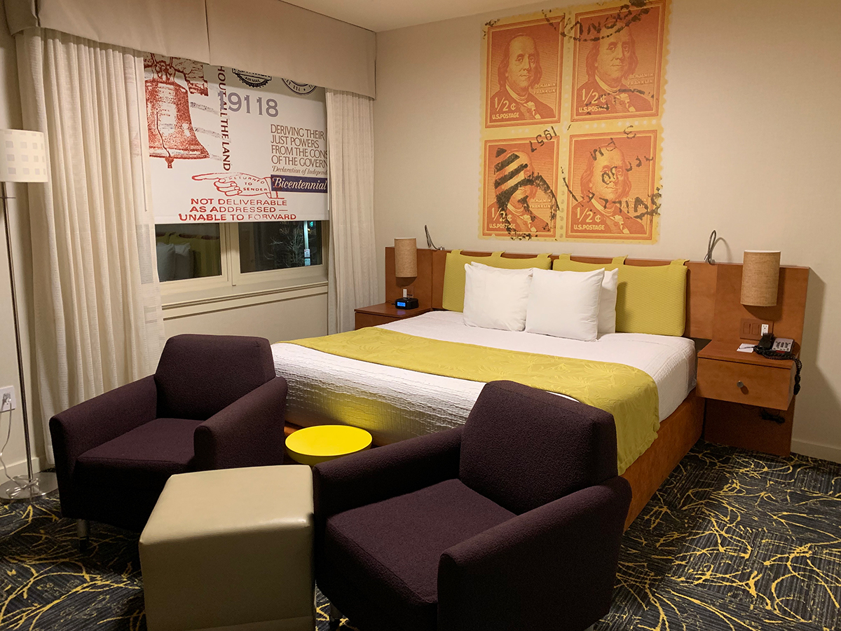 A guest room at Chestnut Hill Hotel that is decorated with vintage postage stamp artwork and deep purple arm chairs.