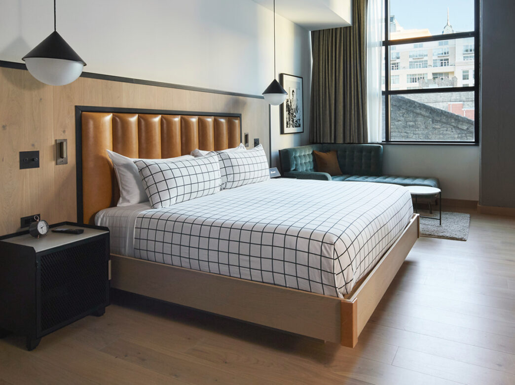 A king guestroom at the Filter Club is decorated with midcentury touches, including windowpane plaid bedding, hanging pendant lights and an alarm clock.