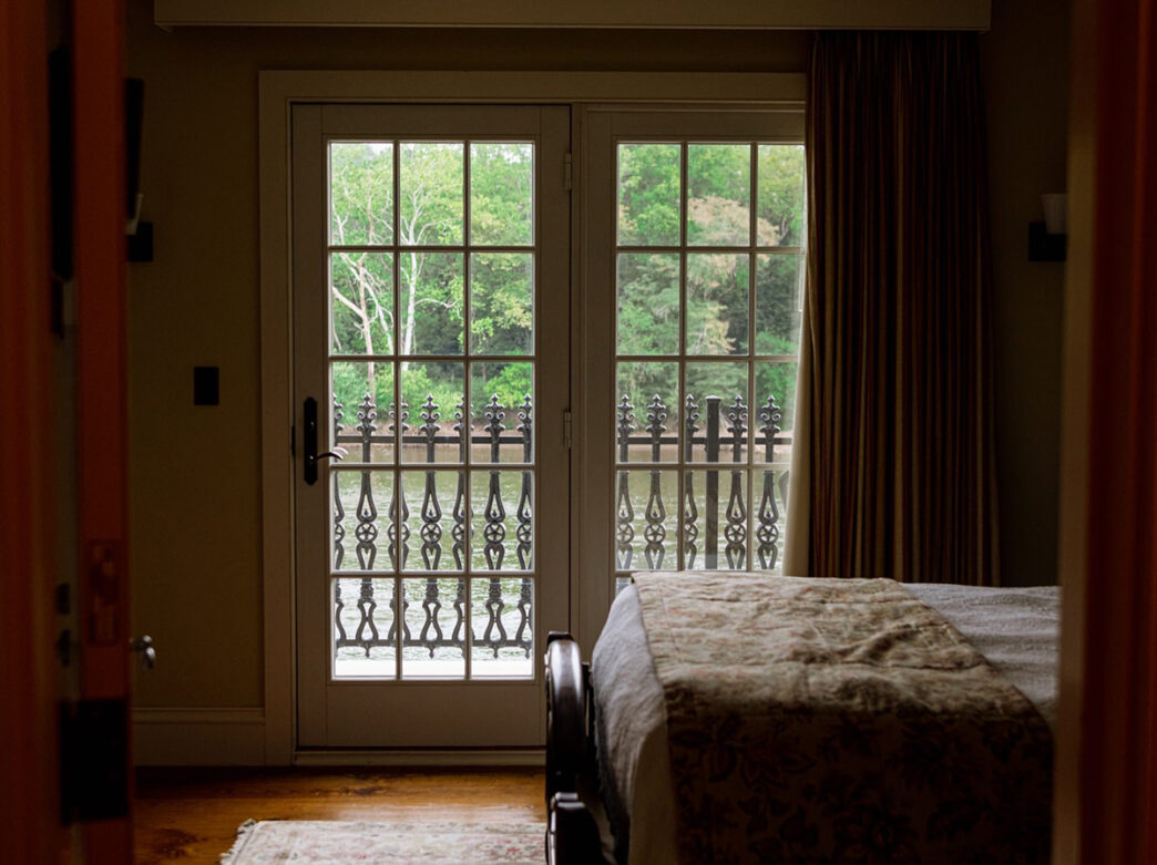 Habitación poco iluminada del Black Bass Hotel con vistas al río Delaware a través de puertas francesas.