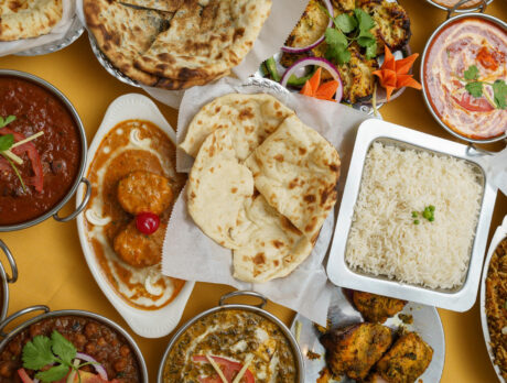 Arroz, naan y una variedad de platos indios se exponen en una mesa con un mantel amarillo.