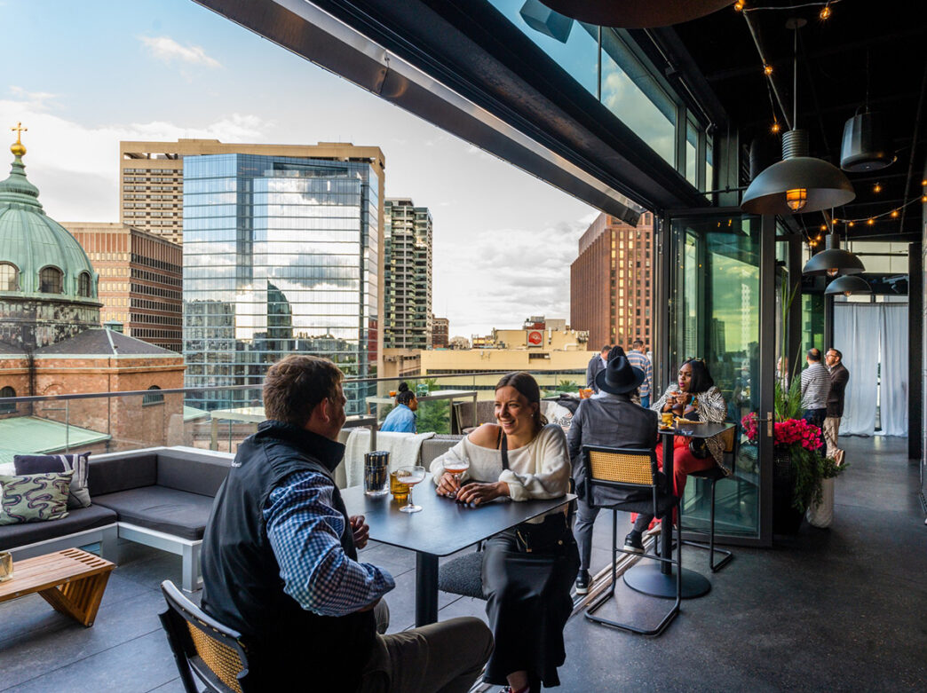 People sit at high top tables and drink cocktails at Assembly Rooftop Lounge.