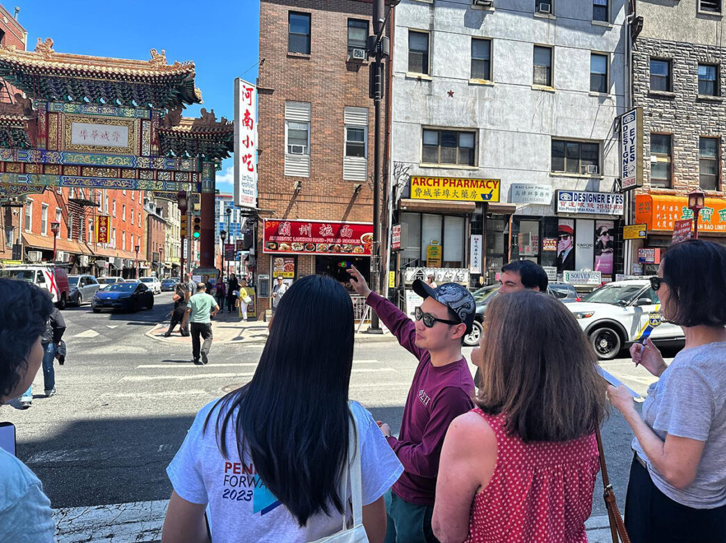 A tour guide points to the Chinatown Gateway Arch while leading a group on food tour through Chinatown.