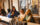 People sit at a bar with cocktails in their hands. Behind them is tufted beige wall panels and curtains.