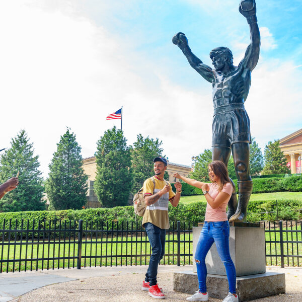 Two people pose in a boxing stance in front of the bronze Rocky Statue at the Philadelphia Museum of Art.