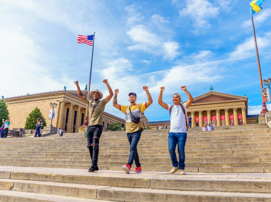 Three people walk down the Art Museum Steps with their hands above their heads like Rocky.