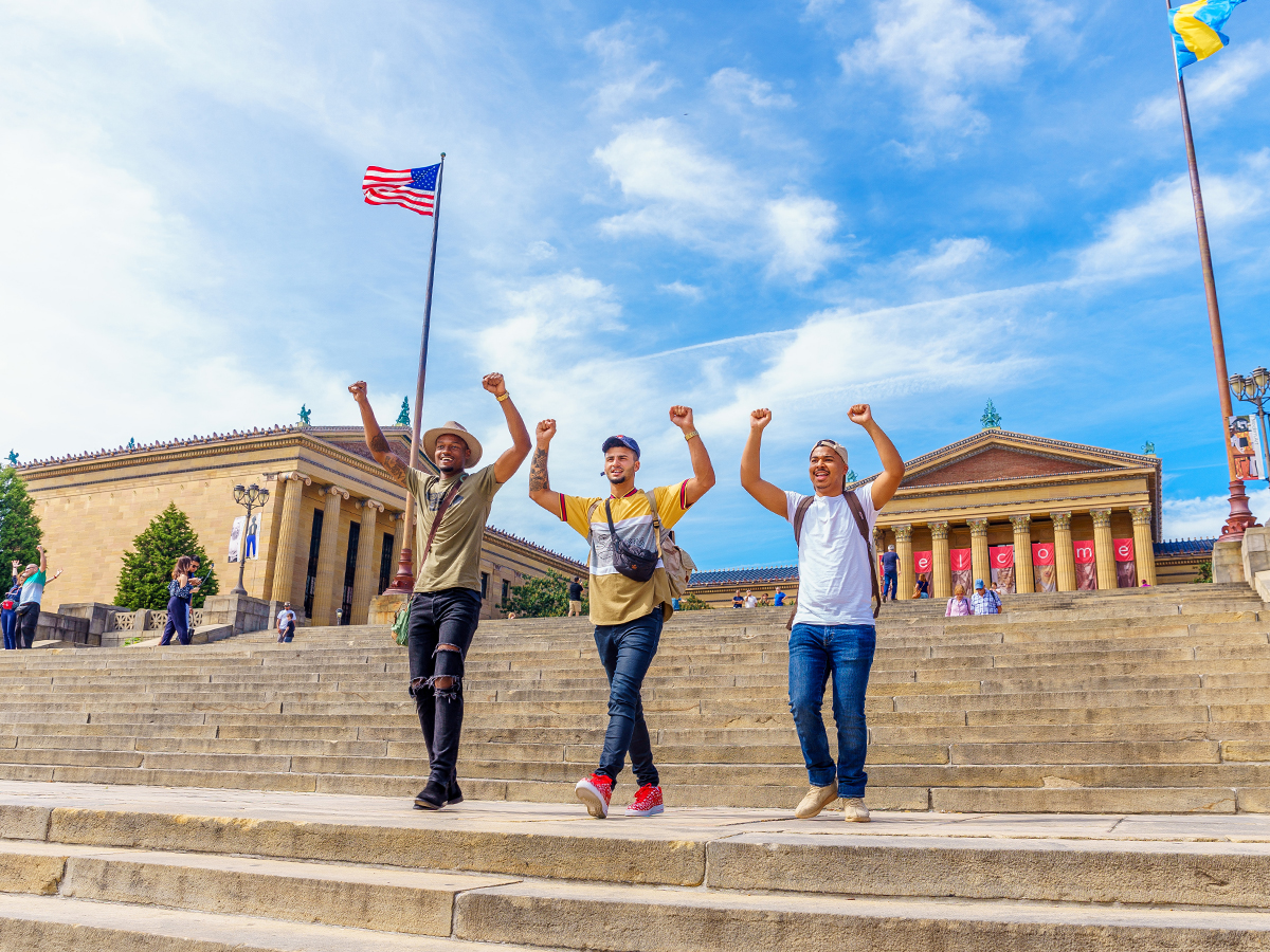 Three people walk down the Art Museum Steps with their hands above their heads like Rocky.
