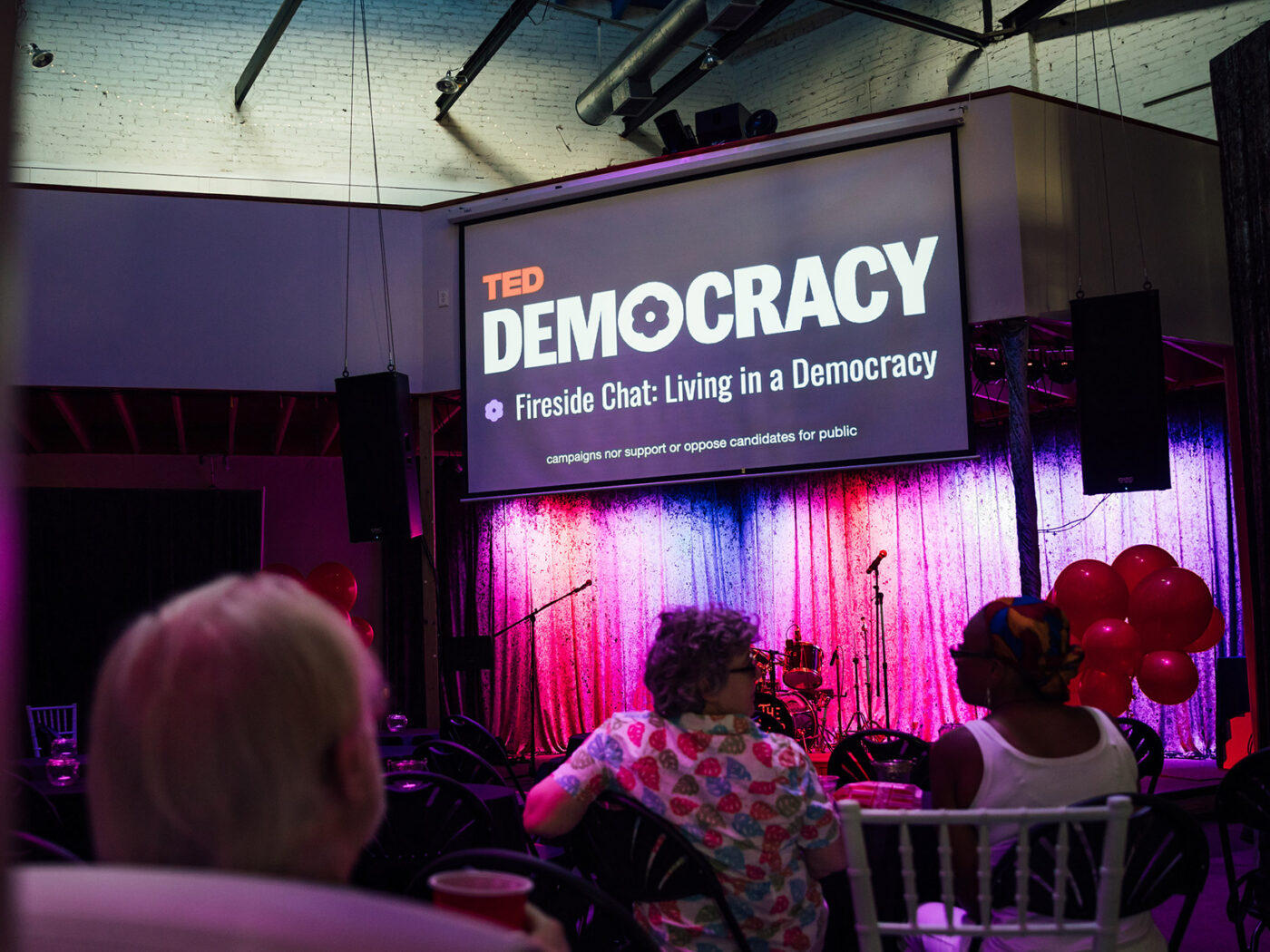 A screen shows the TED Democracy Talk in Philadelphia at a community watch party