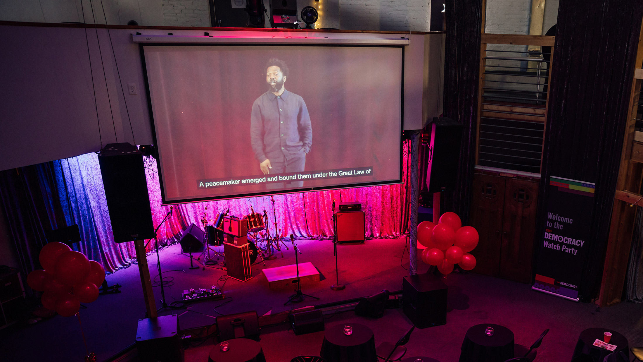 A screen shows the TED Democracy Talk in Philadelphia at a community watch party