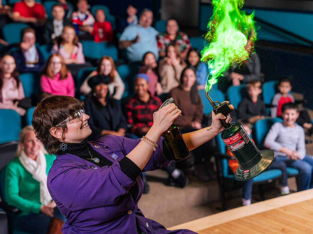 A scientist demonstrating a chemistry experiment with green fire in front of an audience at The Franklin Institute