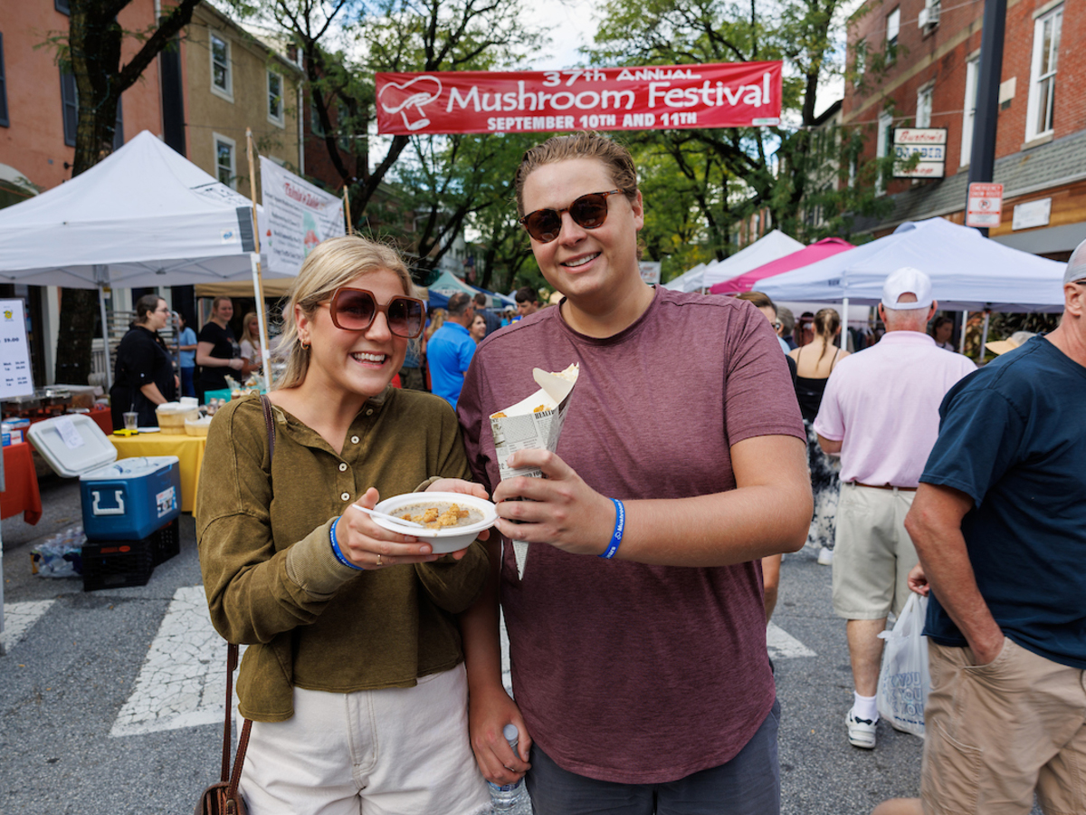 Two people pose for a photo with food bought from vendors at the Kennett Square Mushroom Festival.