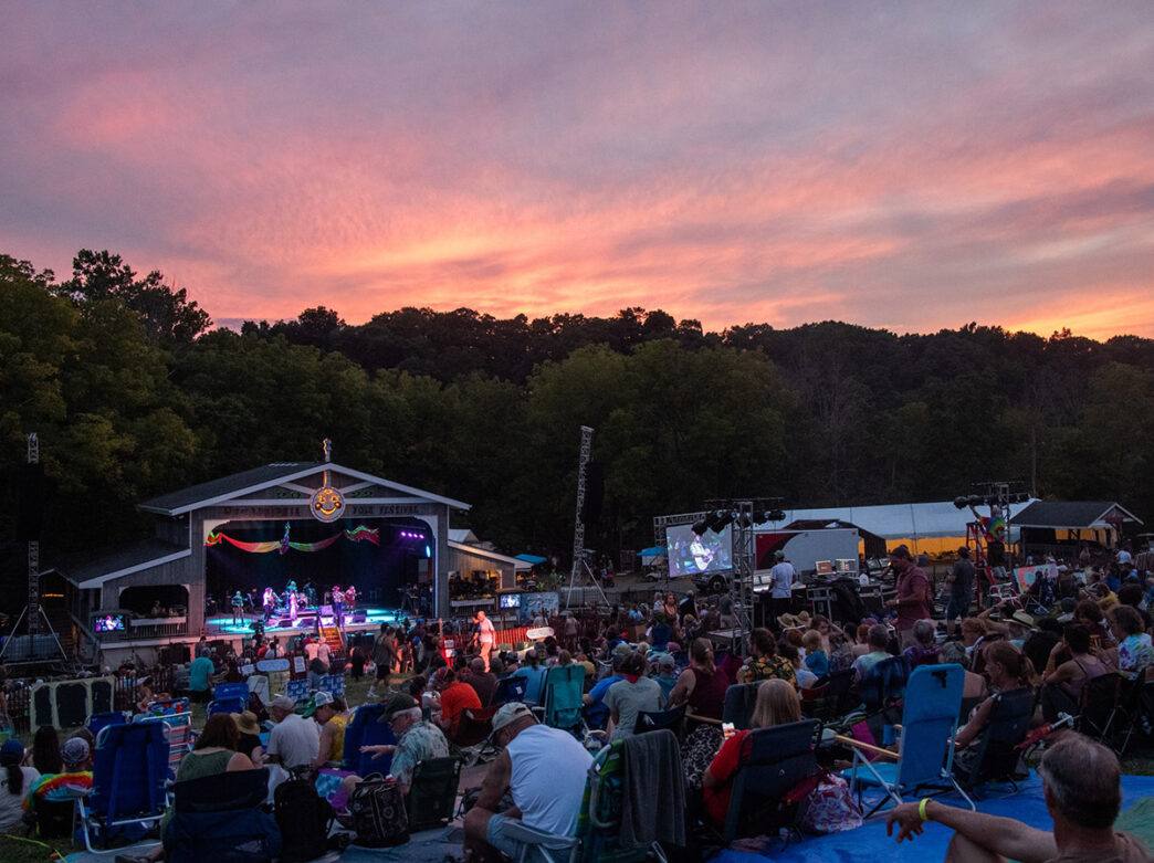 People sitting on the lawn, watching a colorful music performance at the Philadelphia Folk Festival