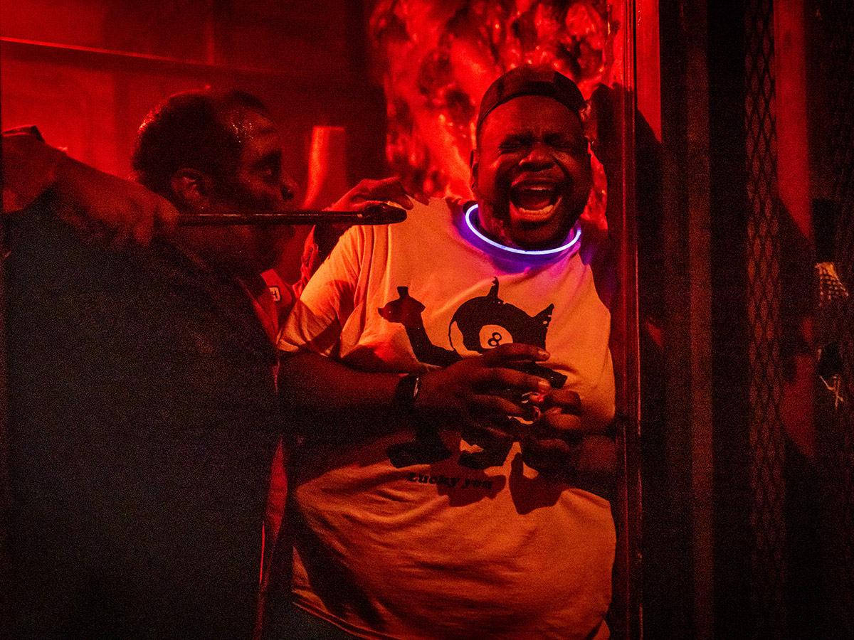 Awash in red light, a scared, screaming visitor is cornered by a haunted house character.