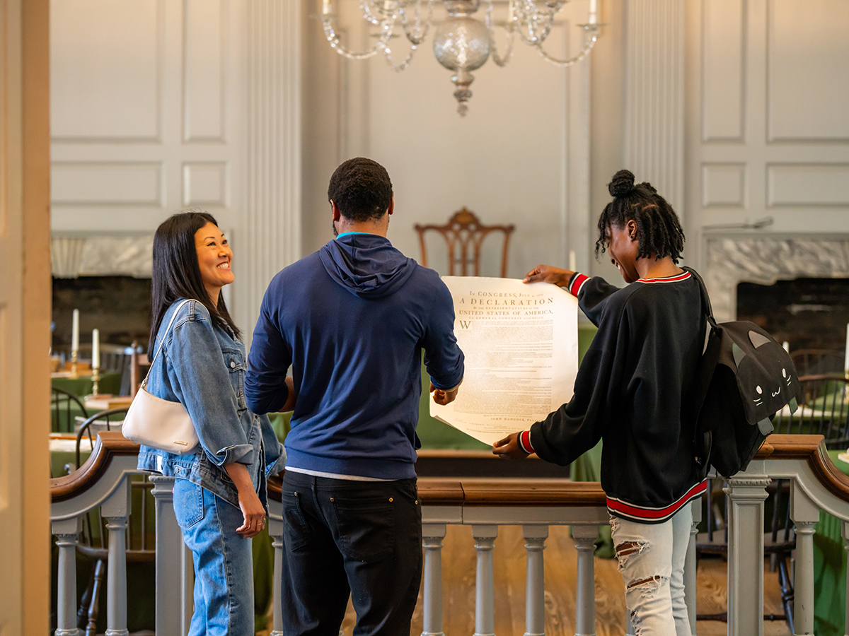 Three people explore the interior of Independence Hall and look at a replica Declaration of Independence.