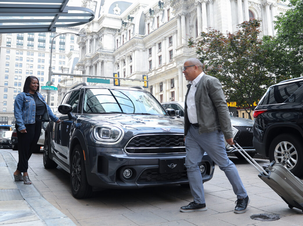 Two guests arrive at the Notary Hotel with a suitcase. City Hall is in the background.