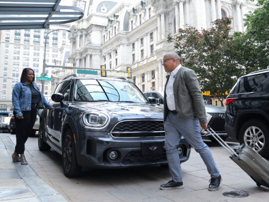 Two guests arrive at the Notary Hotel with a suitcase. City Hall is in the background.