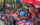 People watching the Puerto Rican Day Parade wave handheld Puerto Rican flags while standing behind a metal fence.