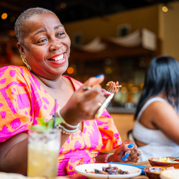 A person wearing a pink and orange dress holds up a forkful of meat while dining at Zahav.
