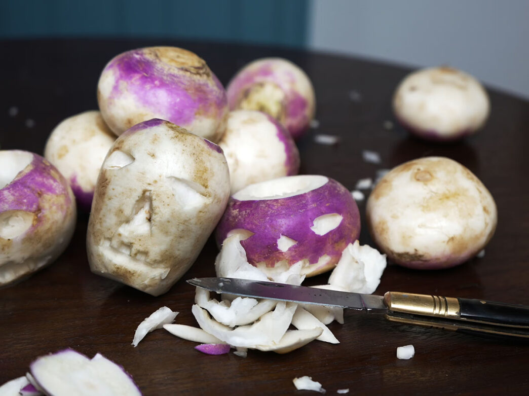 Purple and white turnips with faces carved into them are displayed on a table with a knife.