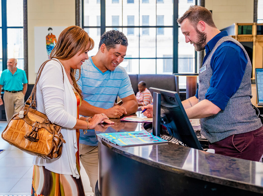Inside the brightly lit lobby of Aloft Hotel, a casually dressed couple checks in with a smartly dressed front-desk employee.