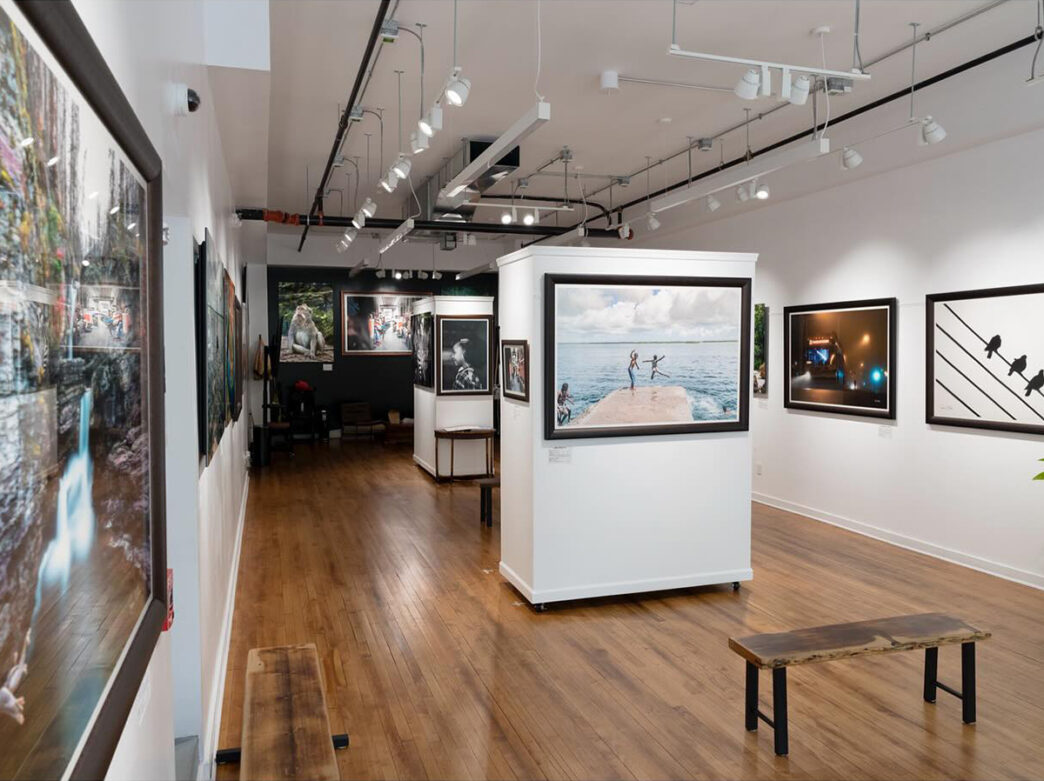 The interior of an art gallery with framed photography hung on the walls and gallery lighting hanging from the ceiling.