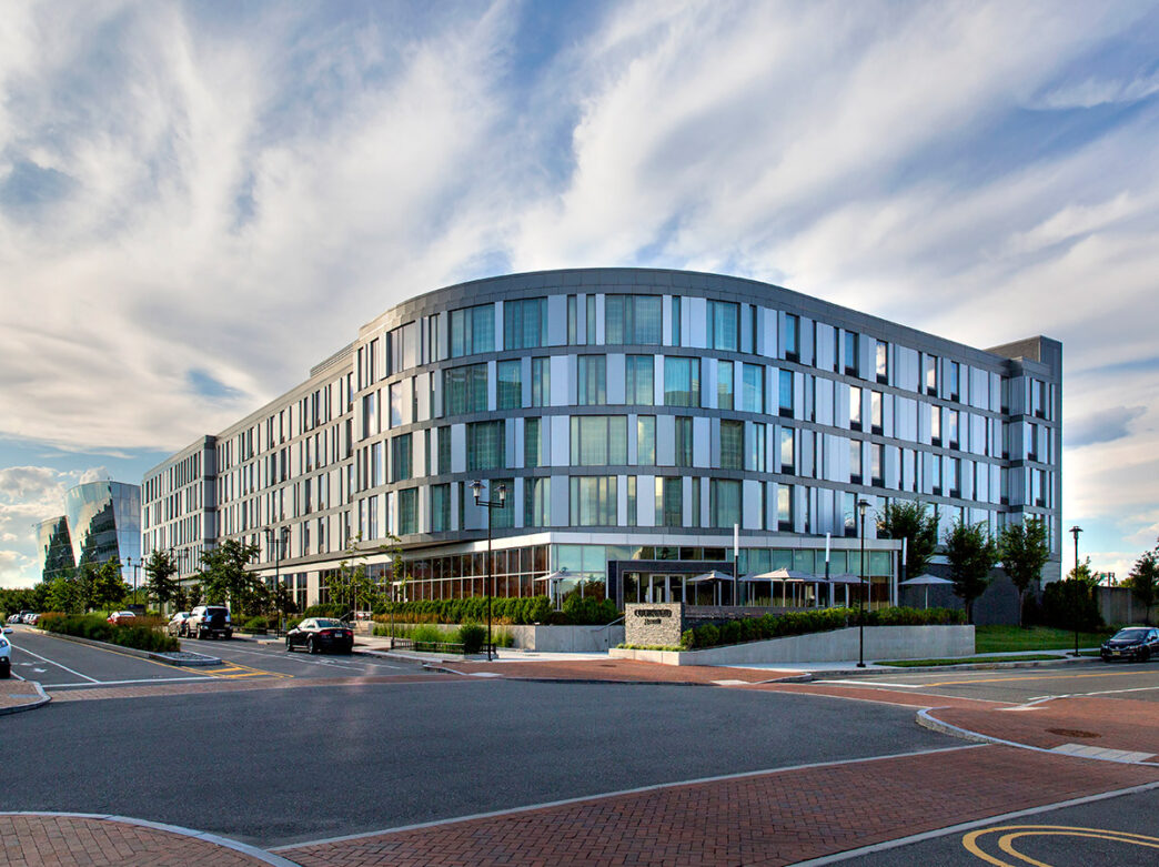 A photo of the Courtyard Philadelphia South hotel at The Navy Yard, a modern, curved building with a gray facade and large windows.