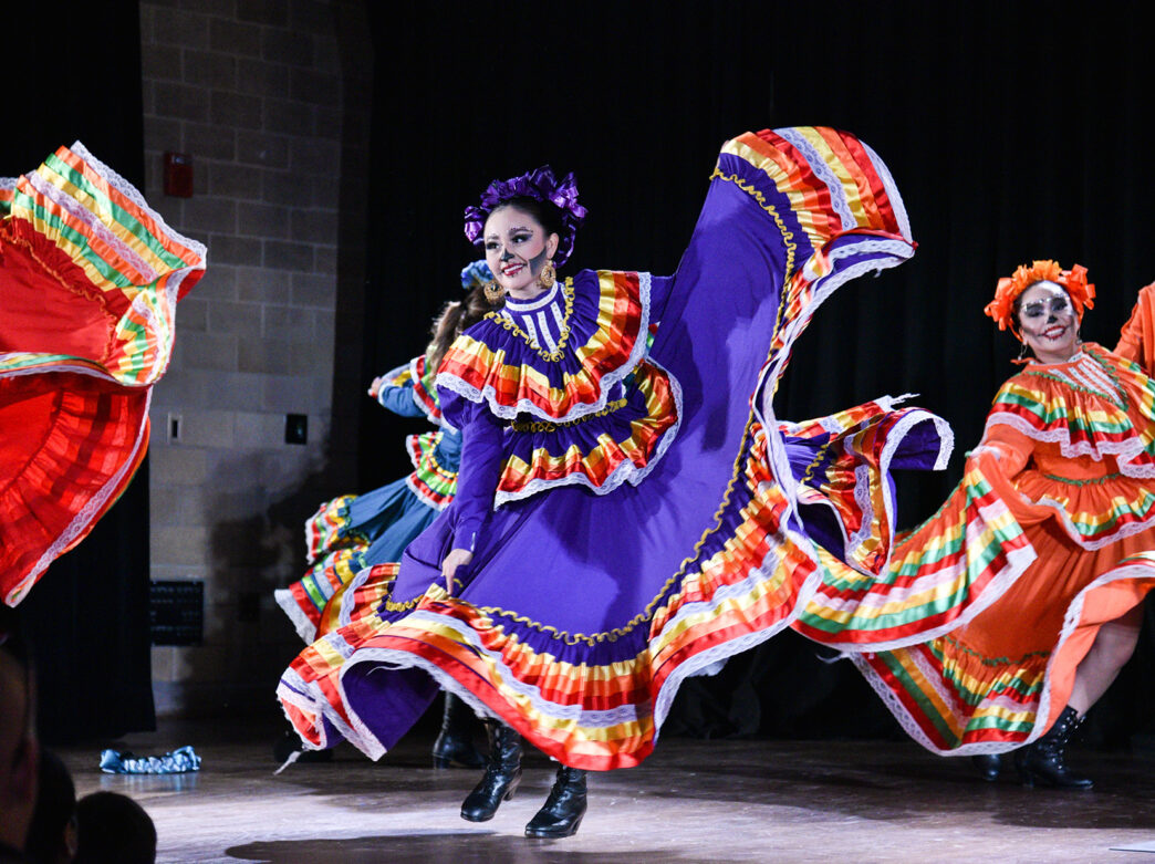 Performers wearing Traditional Mexica dresses dance on stage at CultureFest! Dia de los Muertos at the Penn Museum. The performers faces' are painted with black and white paint to resemble a skull.