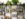 Teas, herbs, elixirs and powders are displayed on a black metal shelf against a white wall. Leafy green plants are on the top shelf.