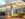 A welcoming hotel entrance featuring a modern arched canopy, a well-lit driveway, and attractive landscaping with colorful flowers and stone accents.