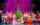 The cast of How the Grinch Stole Christmas The Musical pose for a photo together on stage. An actor dressed as the Grinch is center stage in a green furry costume. The rest of the cast portraying the Whos surround the Grinch in red and white outfits.