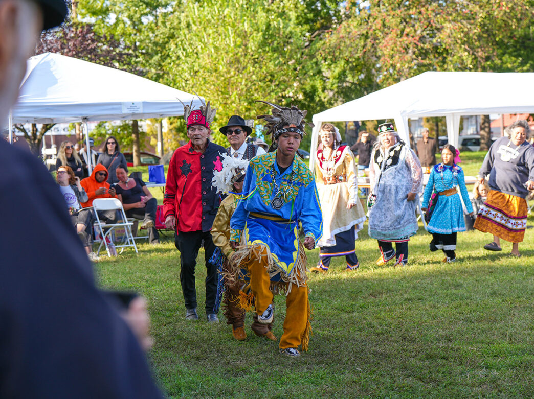 Performers of all ages, dressed in colorful, traditional clothing prepare to perform during an event honoring Indigenous People.