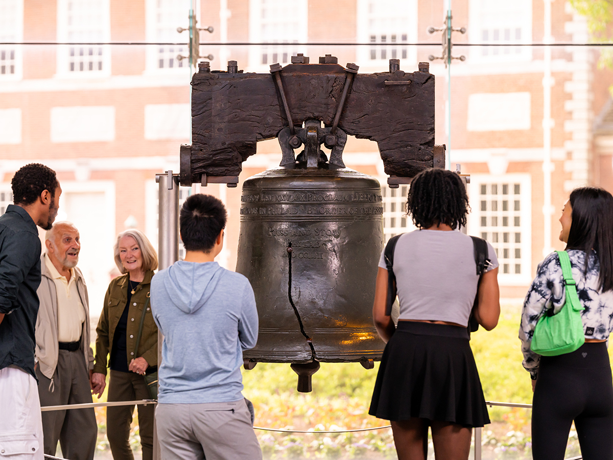 Six people stand around the Liberty Bell and observed it.