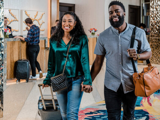 A stylish, smiling couple carries their luggage through the lobby of Live! Hotel.