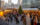 Vendor huts and a large Christmas tree are set up in Love Park for Philadelphia's Christmas Village. People walk around shopping and taking photos. City Hall is in the background.