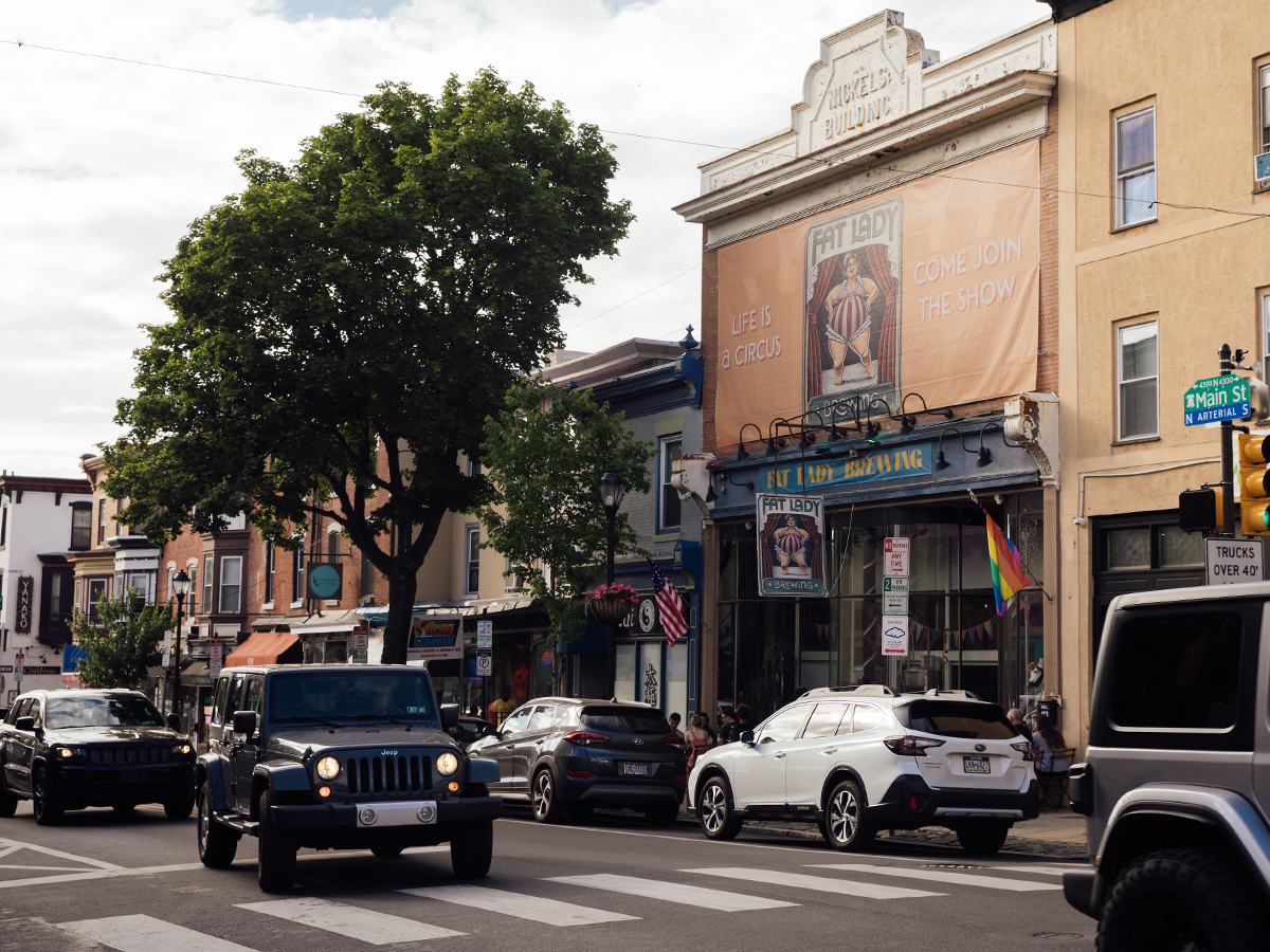 Cars drive down Main Street in Manayunk. Cars are parallel parked with stores and shops lining the street.