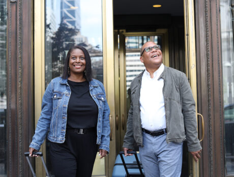 A smiling couple sporting jean jackets and casual outfits walk out the glass doors of The Notary.