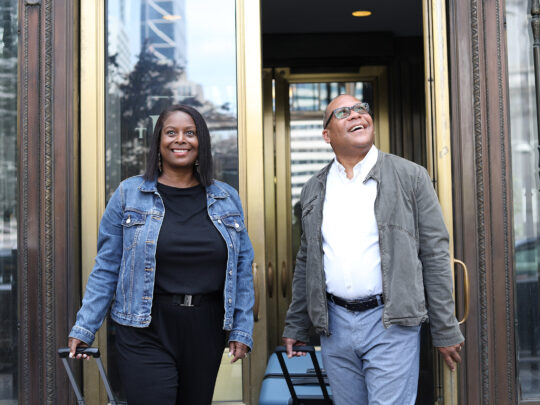 Un couple souriant, vêtu de vestes en jean et de tenues décontractées, sort par les portes vitrées du Notary.