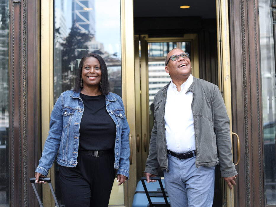 A smiling couple sporting jean jackets and casual outfits walk out the glass doors of The Notary.