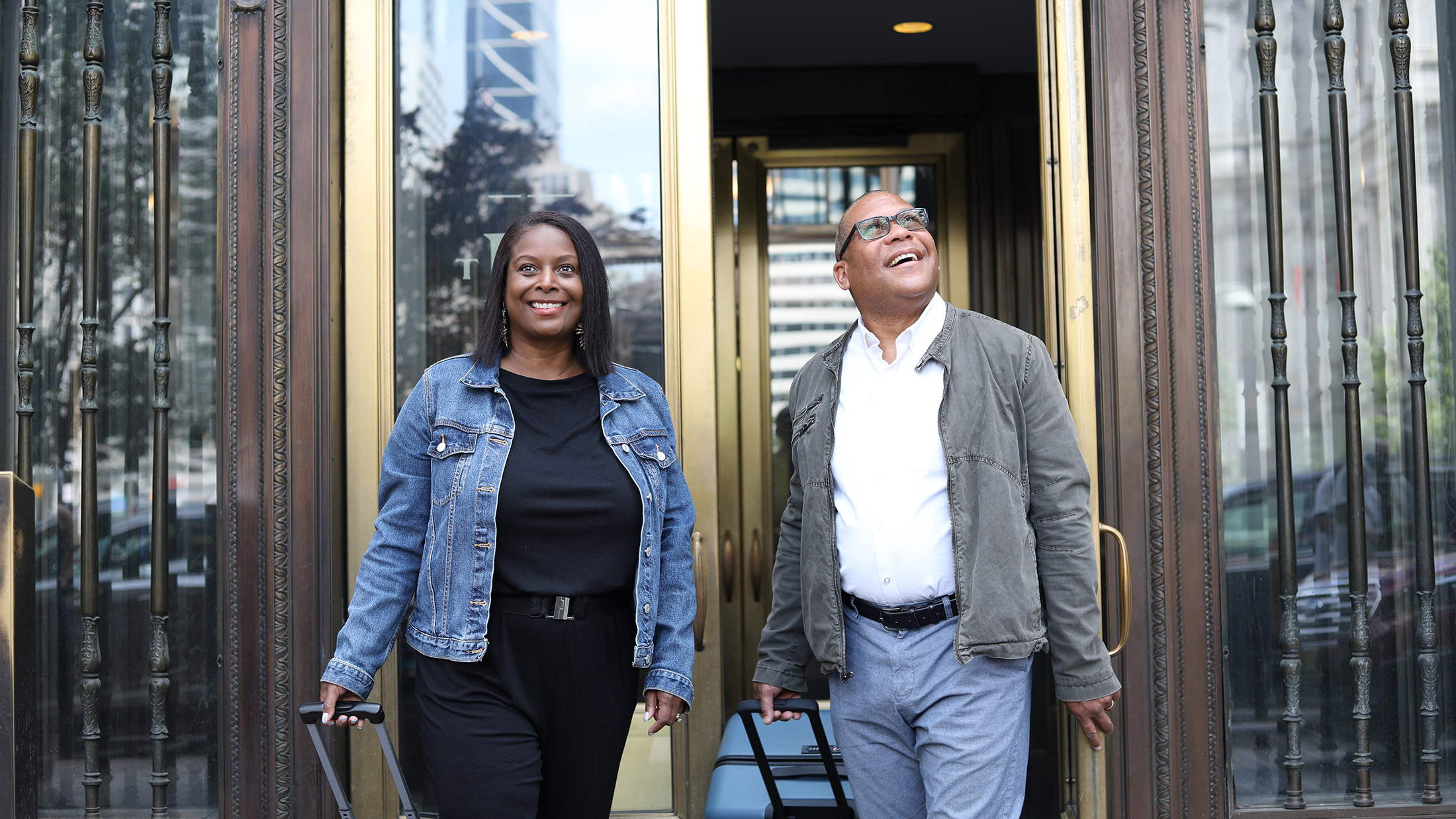A smiling couple sporting jean jackets and casual outfits walk out the glass doors of The Notary.