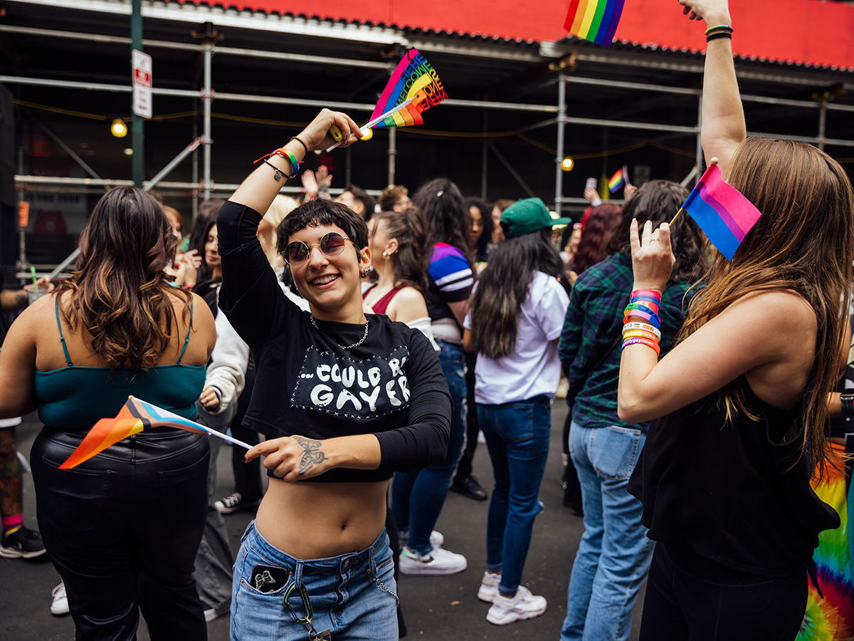 Une personne danse joyeusement avec un drapeau arc-en-ciel dans chaque main au milieu d'une foule lors du festival OURFest à Philadelphie.