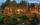 A panoramic view of Peddler's Village at twilight, showcasing a variety of trees and buildings illuminated with colorful holiday lights. A gazebo adorned with white lights stands in the background.