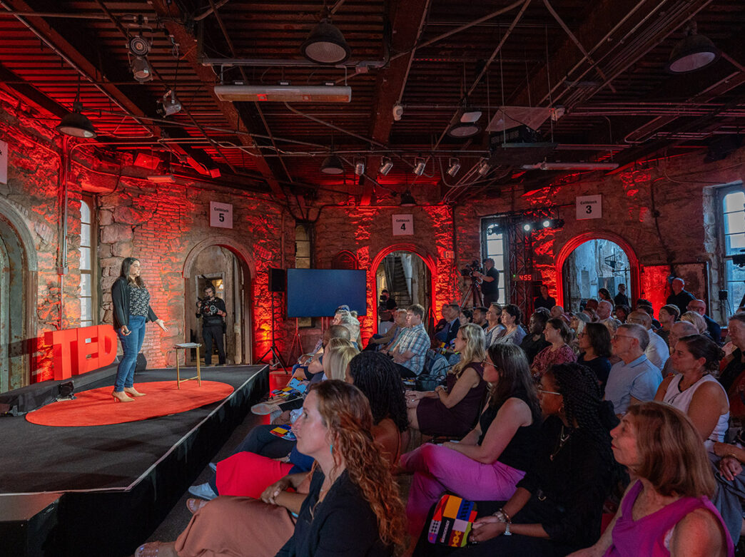 A person standing on a small stage addresses a crowd of people during a TED Democracy Fireside Chat at Eastern State Penitentiary in Philadelphia