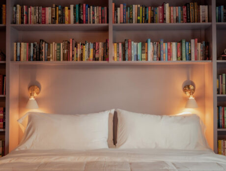 A bed with white sheets and pillows, flanked by built-in bookshelves and illuminated by wall-mounted reading lamps.