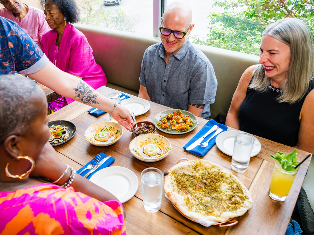 A server places a dish between smiling patrons seated at a table.
