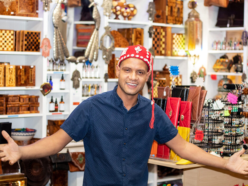 Chakir Bouchaib, owner of Little Marrakesh Bazaar, poses for a photo in his shop in Reading Terminal. Behind him there are handcrafted goods displayed.