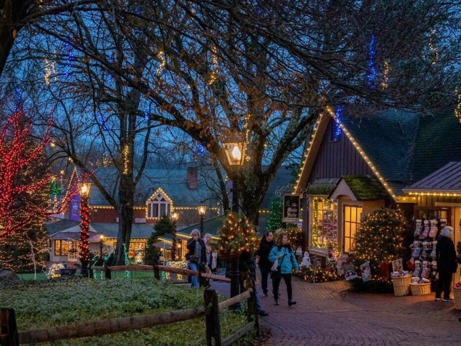 People strolling through Peddler's Village with holiday lights decorating the trees and buildings.